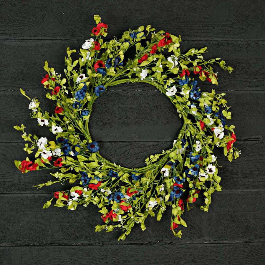 Decorative wreath with red, white, and blue flowers on a black wooden background