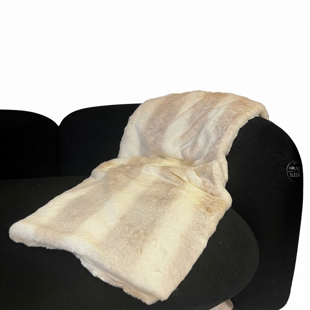 White faux fur blanket draped over a black chair against a dark wall with a plant in the corner.