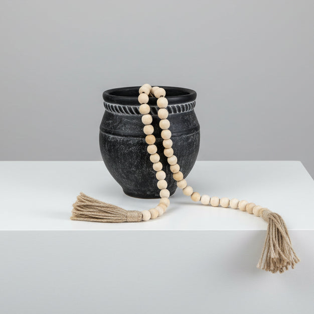 Black stone bowl with a white beaded necklace and tassels on a white background