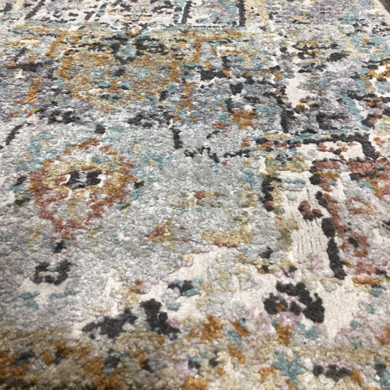 A close-up of a textured area rug with an abstract, distressed pattern in shades of gray, beige, black, rust orange, and muted blue.