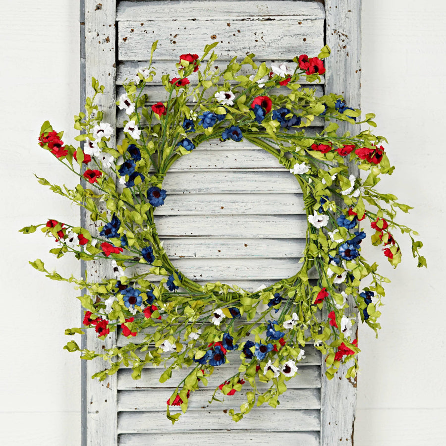 Floral wreath with red, blue, and white flowers on a wooden door.