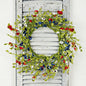 Floral wreath with red, blue, and white flowers on a wooden door.