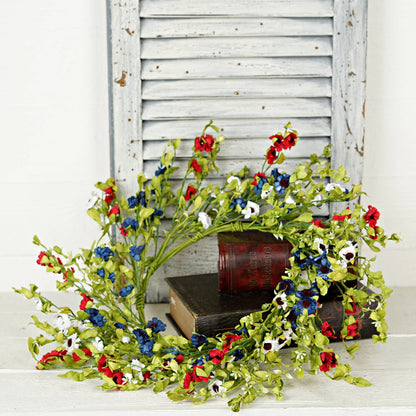 Decorative floral branch with red, blue, and white flowers on a wooden surface with a white shutter background.
