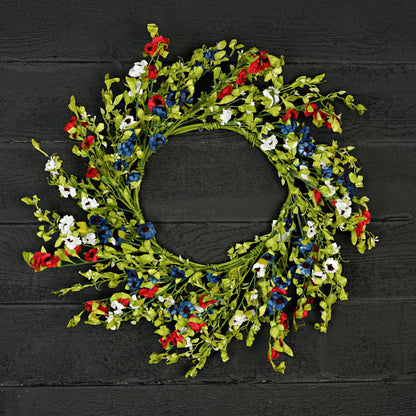 Decorative wreath with red, white, and blue flowers on a black wooden background