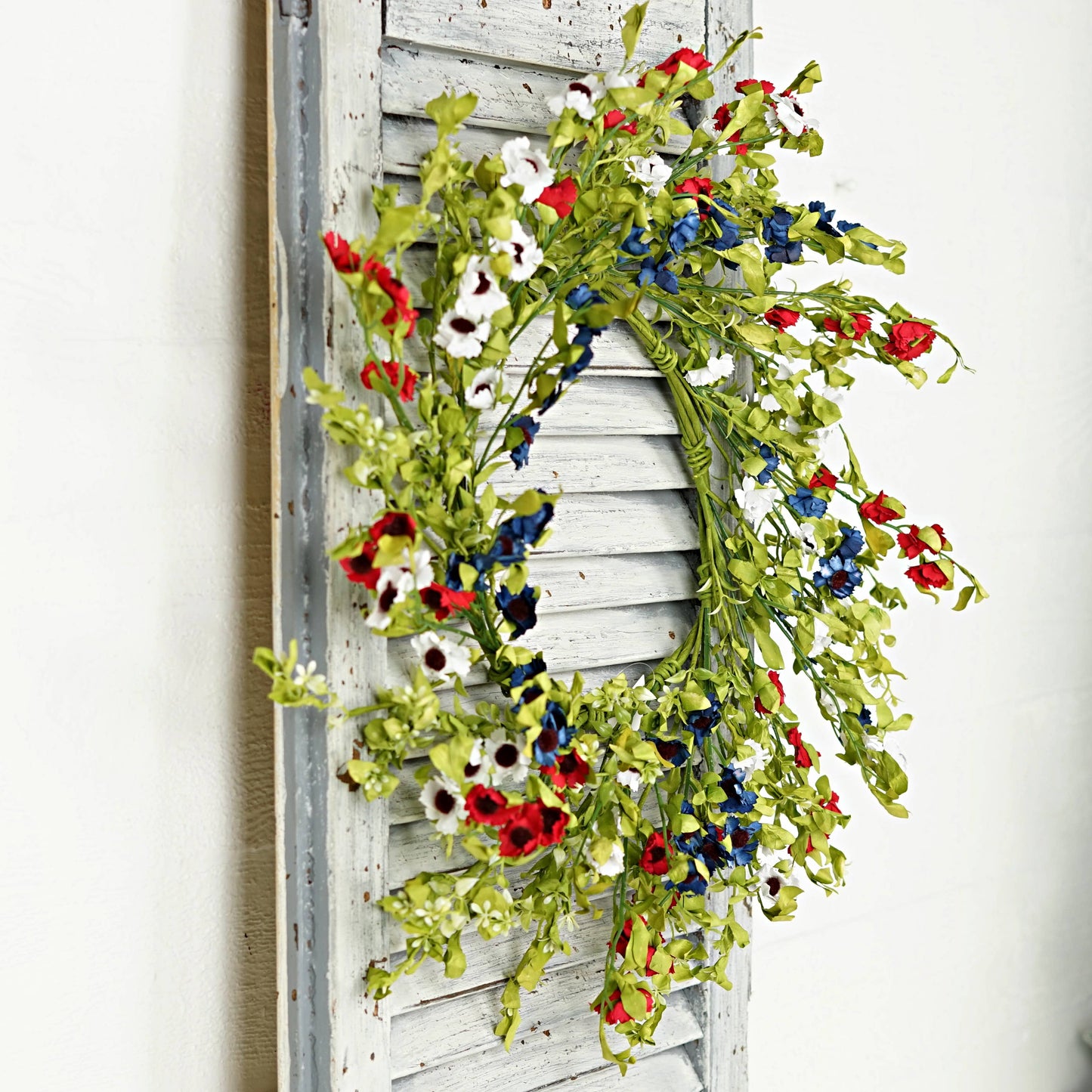 Floral wreath with red, white, and blue flowers on a wooden shutter.