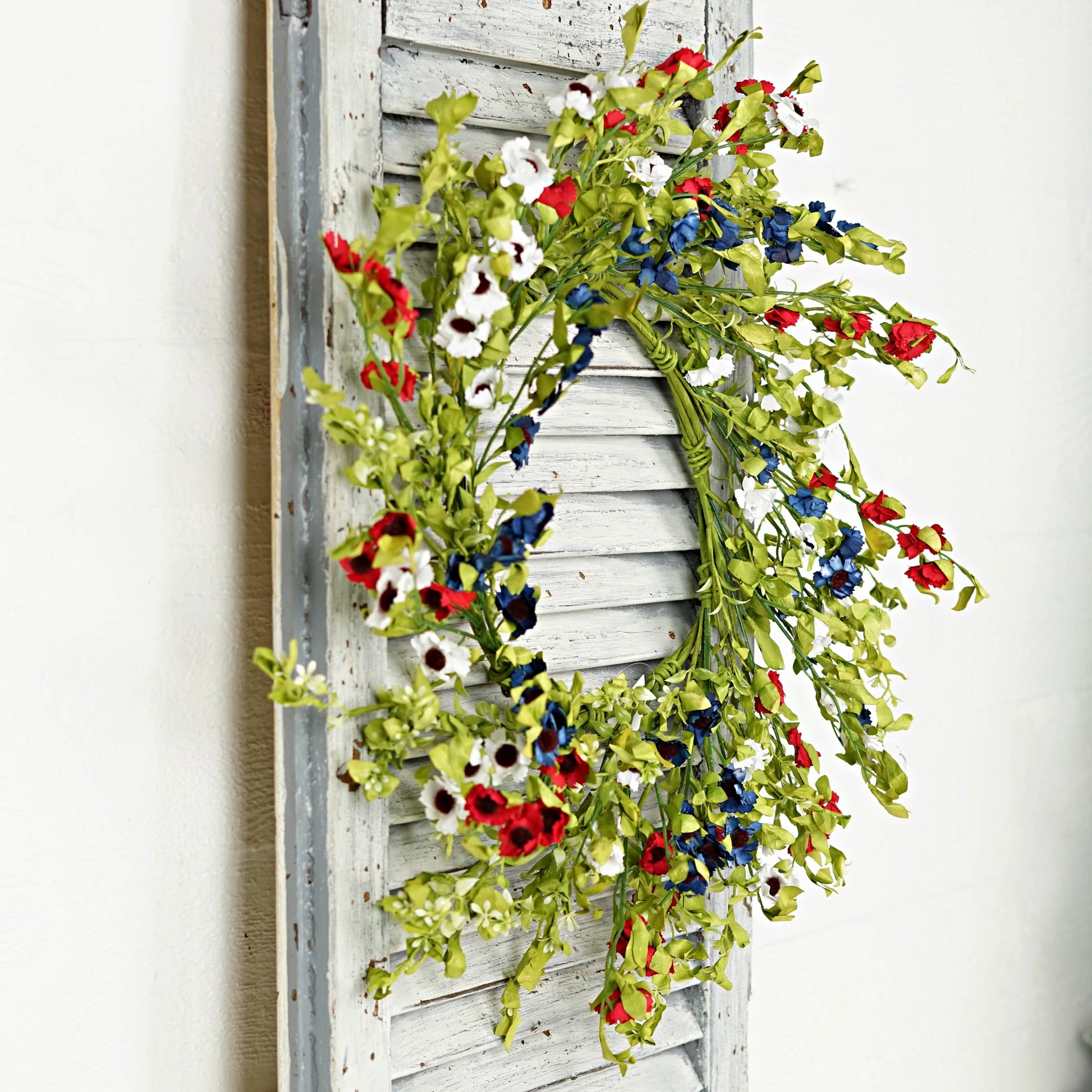 Floral wreath with red, white, and blue flowers on a wooden shutter.