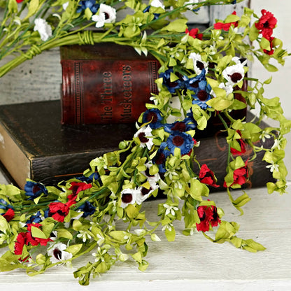 Artificial floral garland with red, white, and blue flowers on a wooden surface.