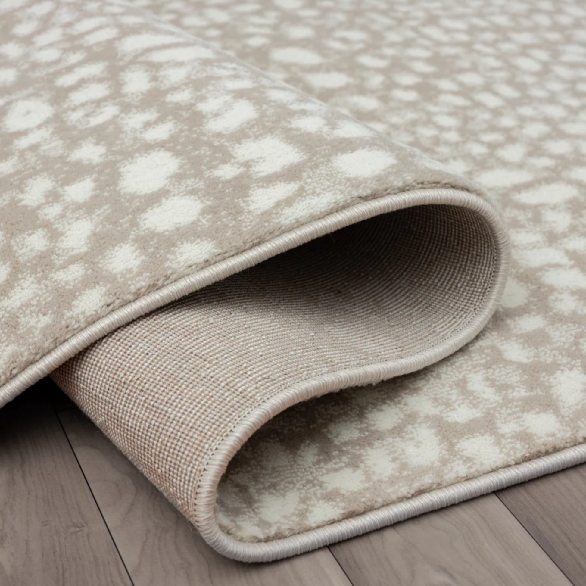 A close-up of a rolled area rug with a beige and off-white animal print pattern, shown on a gray wood plank floor.