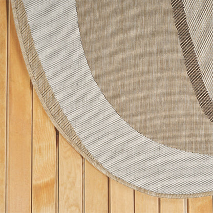 A close-up of a woven oval rug with a thick cream border and a tan center, laid over a light wood plank floor.