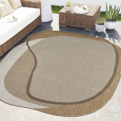 An abstract-shaped outdoor area rug in beige and brown tones, shown on a patio in a furnished backyard setting with a wicker sofa, coffee table, and potted plants.