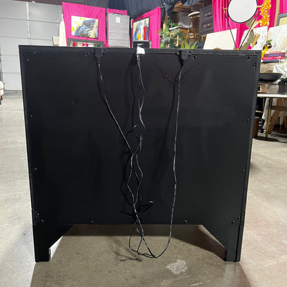Black metal cabinet with wires on a concrete floor, with a blurred background of a store interior.