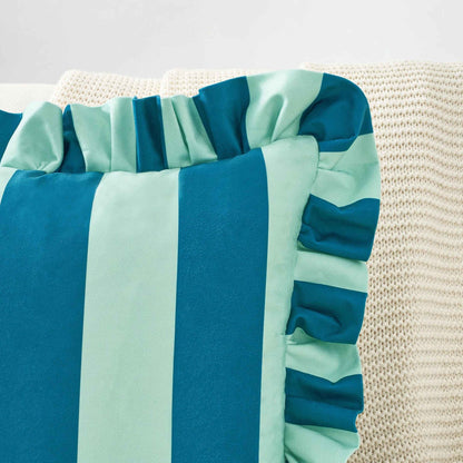 A striped throw pillow in blue and light blue with a ruffled edge, resting on a cream-colored knit blanket.