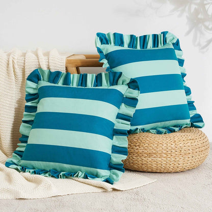 Two striped throw pillows with ruffled edges in shades of blue and light blue, styled on a beige knit blanket next to a woven basket.