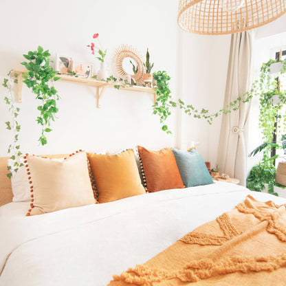 Cozy bedroom with a bed featuring colorful pillows and a shelf with plants.
