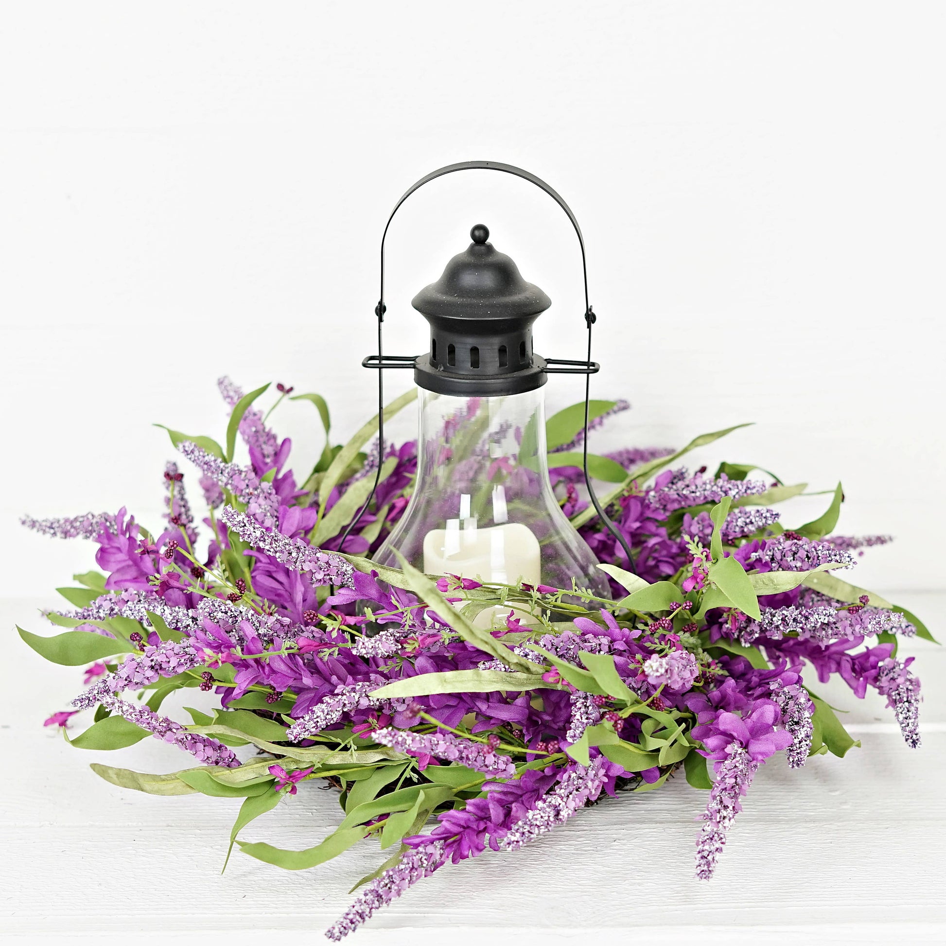 Decorative arrangement with purple flowers, green leaves, and a black lantern on a white background