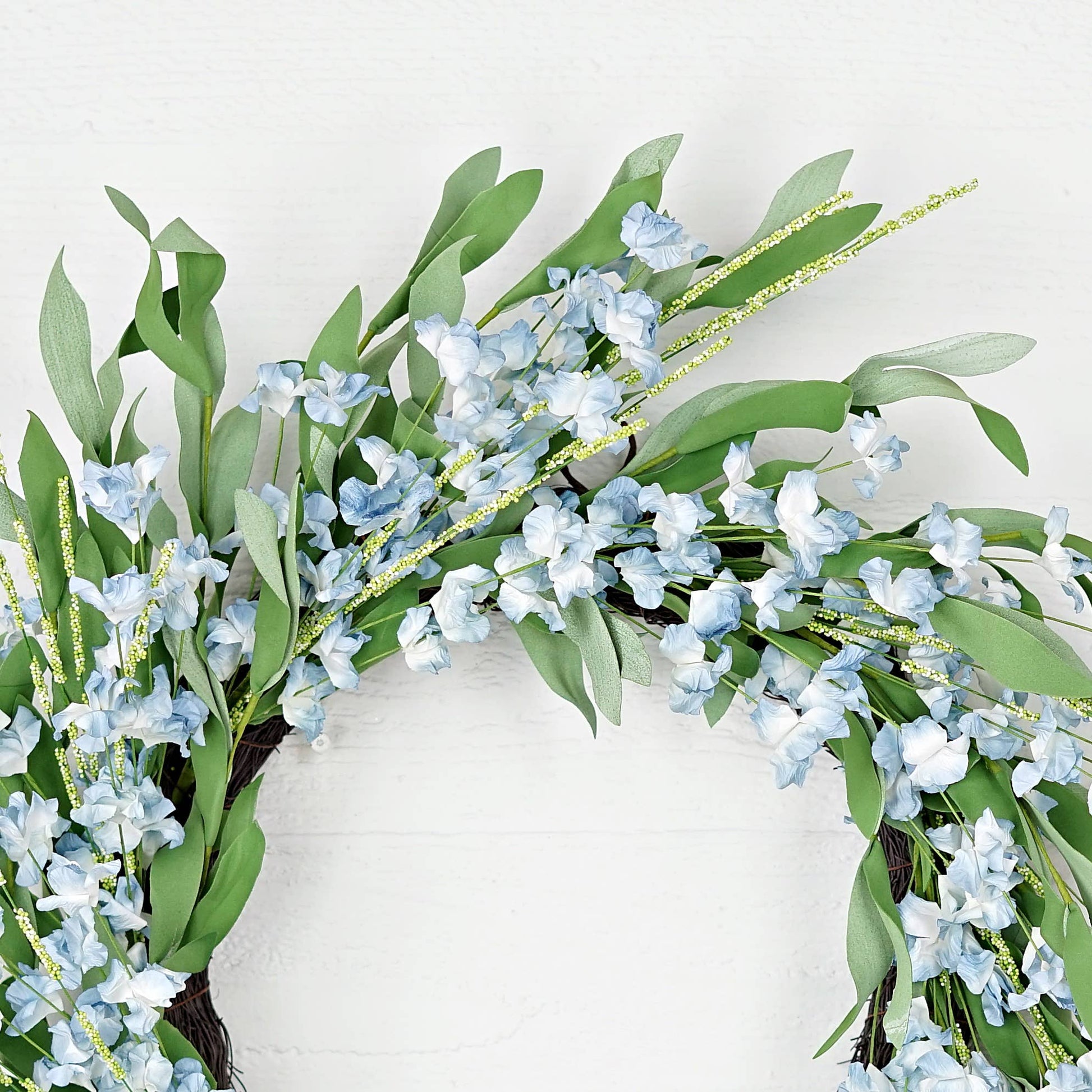 Decorative wreath with green leaves and small blue flowers on a white background