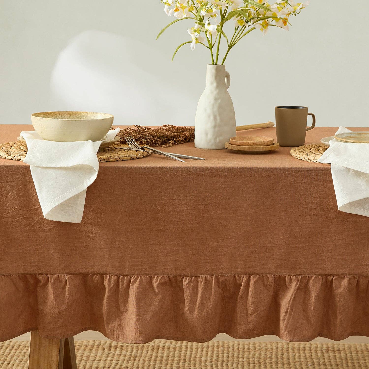 Dining table set with a brown tablecloth, white vase with flowers, and ceramic items.