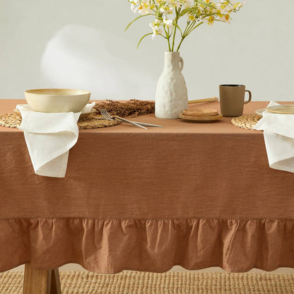 Dining table set with a brown tablecloth, white vase with flowers, and ceramic items.