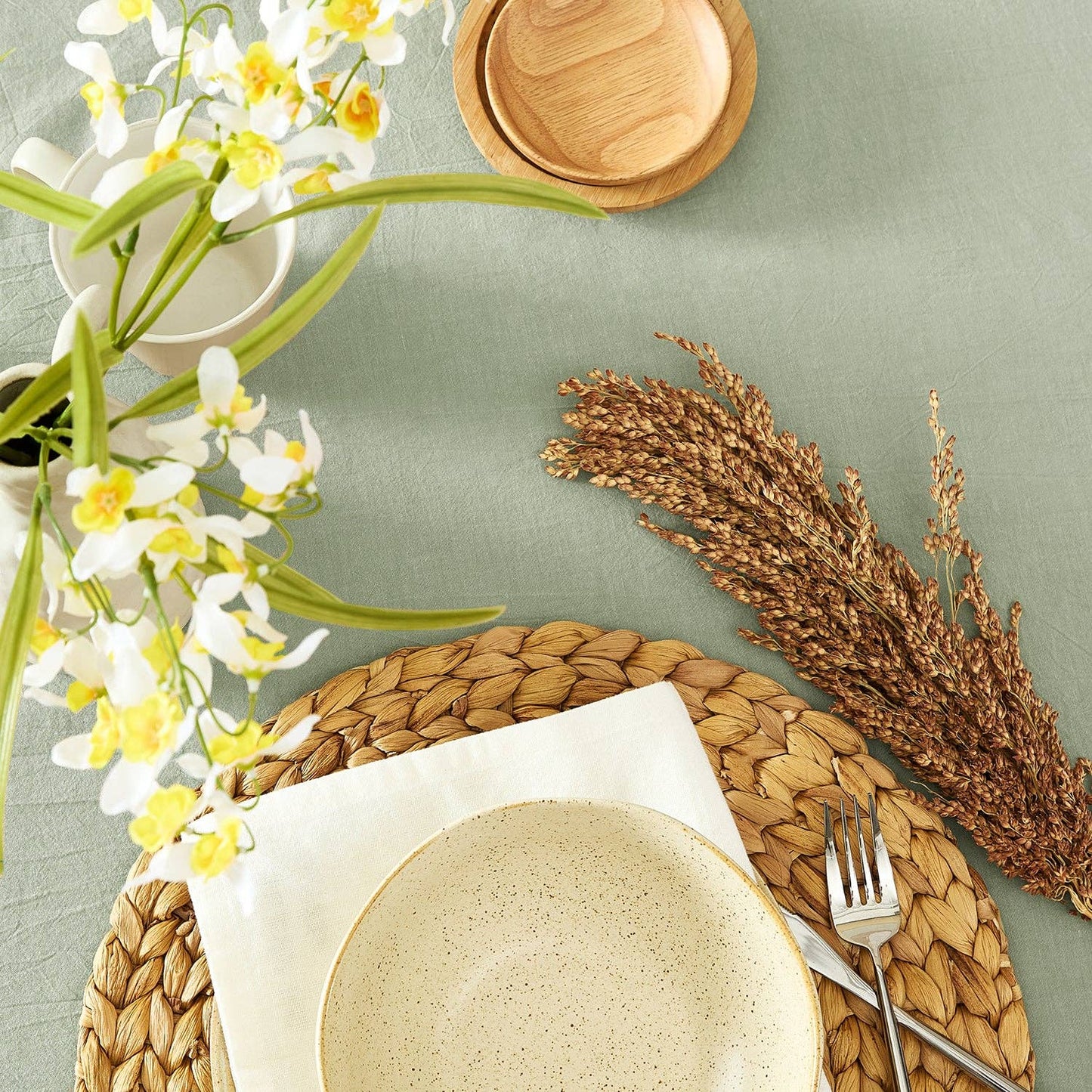 Dining table setting with plates, flowers, and wheat on a light green surface