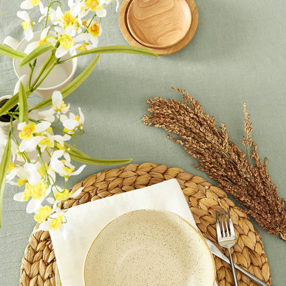 Dining table setting with plates, flowers, and wheat on a light green surface