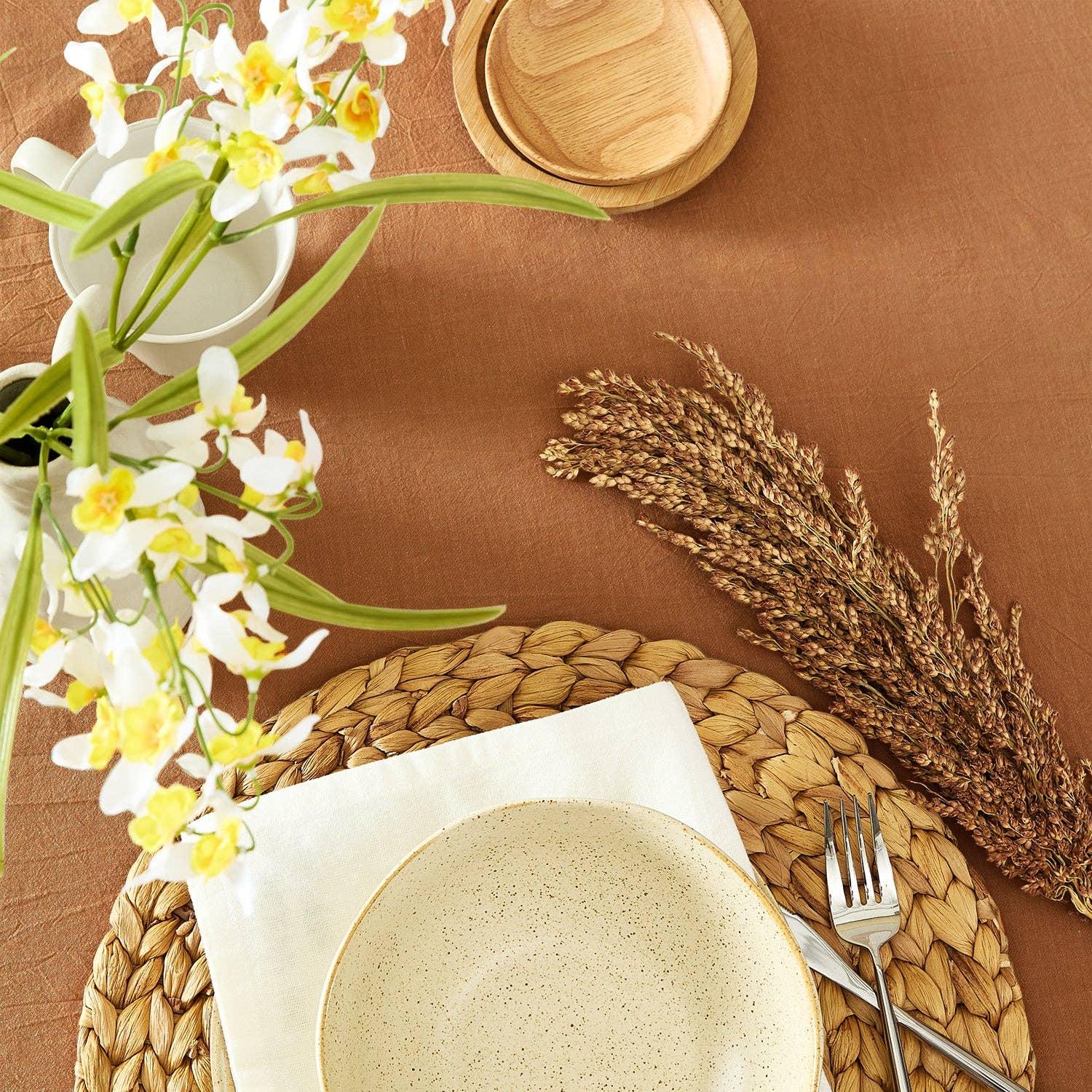 Dining table setting with plates, flowers, and cutlery on a brown surface
