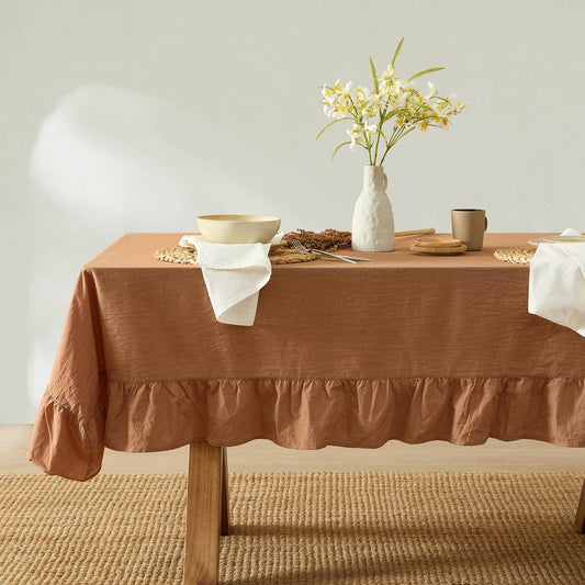 Dining table with a brown tablecloth, white vase with flowers, and various items on a neutral background