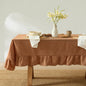 Dining table with a brown tablecloth, white vase with flowers, and various items on a neutral background