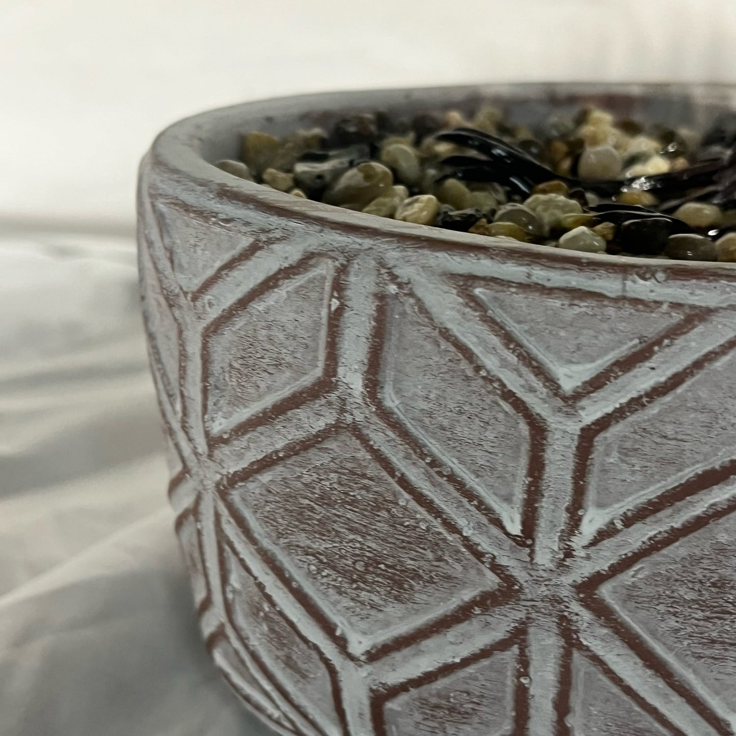 Ceramic pot with geometric pattern filled with pebbles on a white background