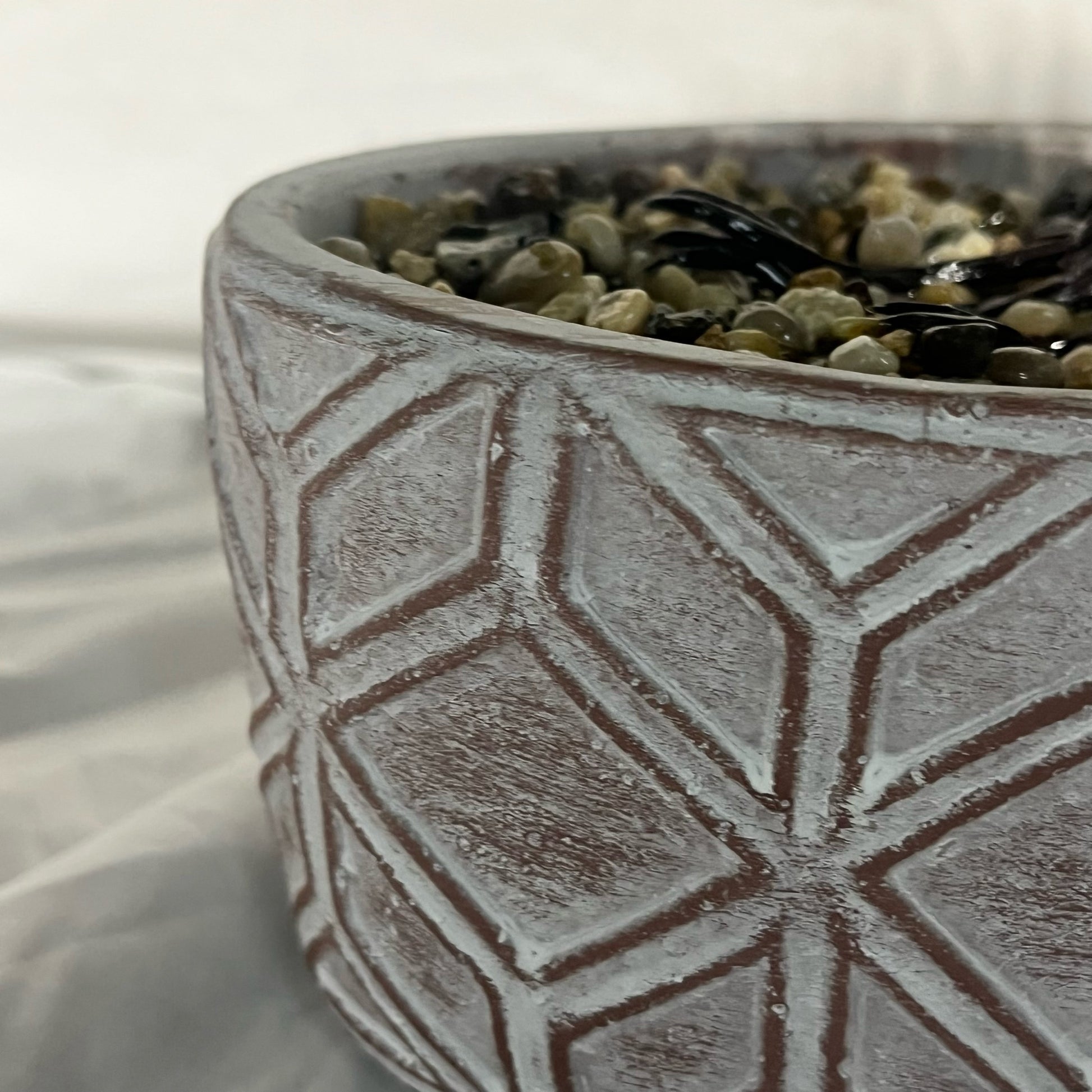 Ceramic pot with geometric pattern filled with pebbles on a white background