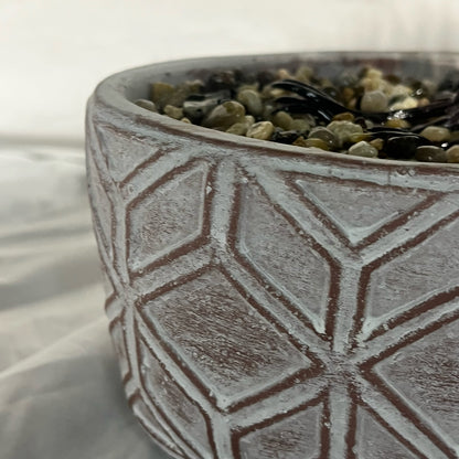 Ceramic pot with geometric pattern filled with pebbles on a white background