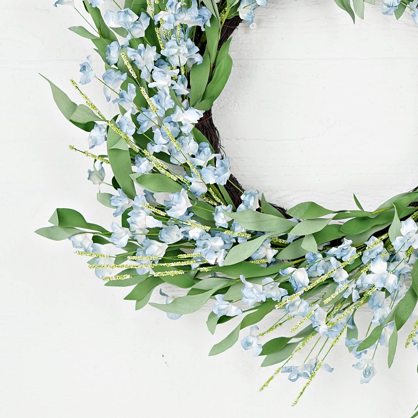 Floral wreath with blue flowers and green leaves on a white background
