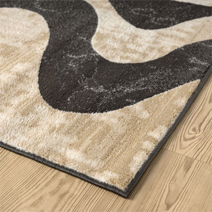 A close-up of a textured area rug with an abstract wavy pattern in beige and dark charcoal gray, shown on a light wood floor.