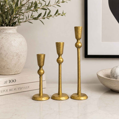 Three gold candle holders on a table.