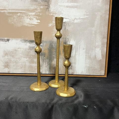 Three gold candle holders on a table.