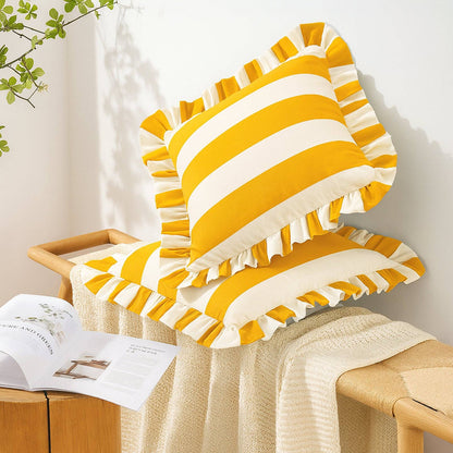 Yellow and white striped pillows on a wooden stool with a book and plant in the background