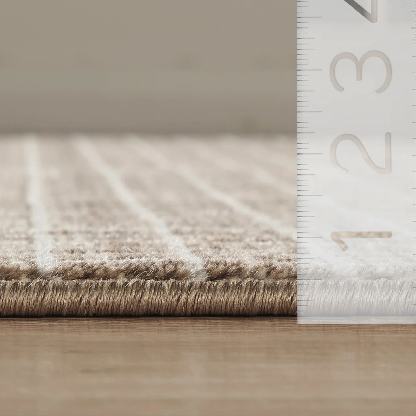 Close-up of a beige textured rug, shown on a wooden floor next to a white ruler for scale.