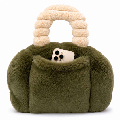 An moss green faux fur Pur-low with a chunky cream-colored handle, featuring a front pocket holding a smartphone, set against a plain white background.