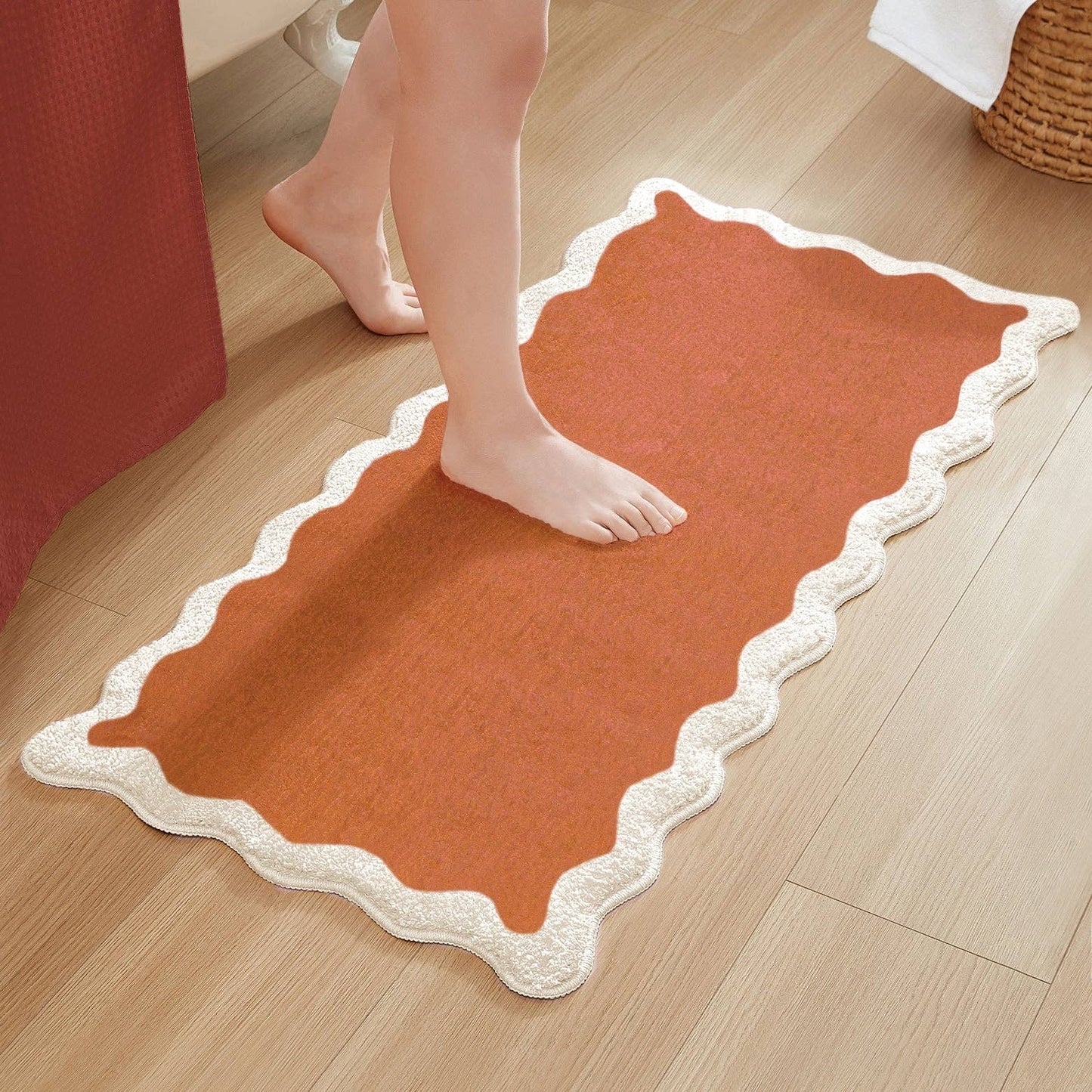Orange bath mat with scalloped edge on a wooden floor