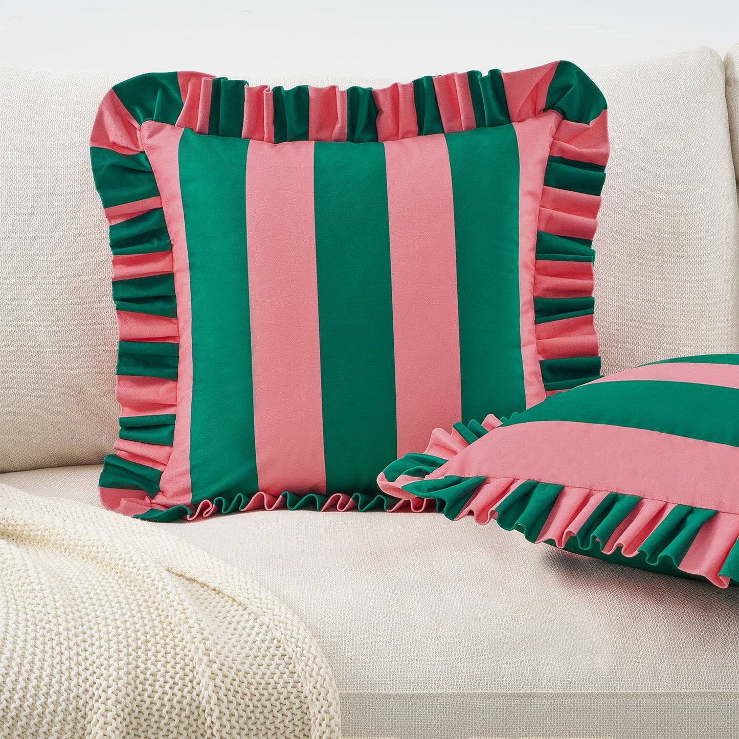 Striped pink and green pillow with ruffled edges on a beige sofa.