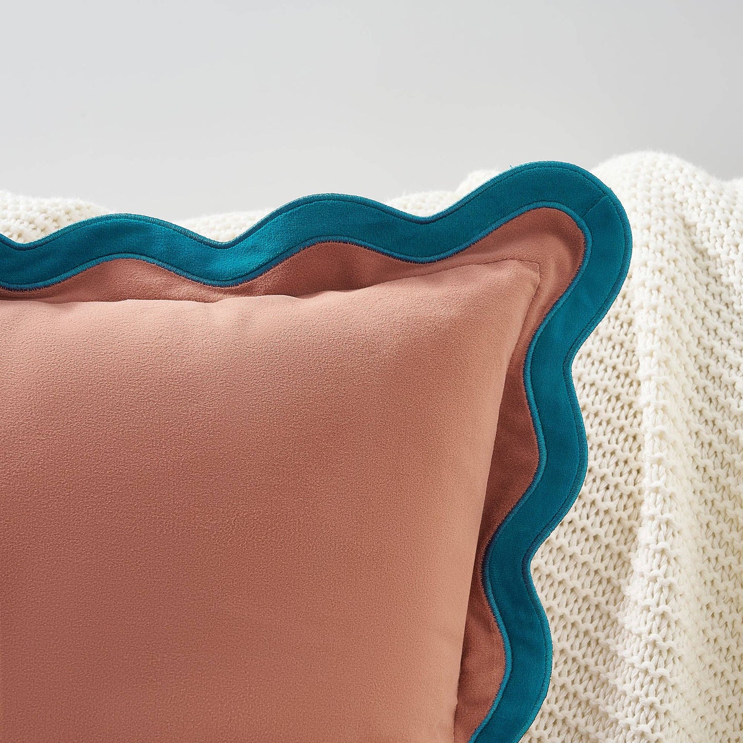 Pink pillow with teal scalloped edge on a textured surface