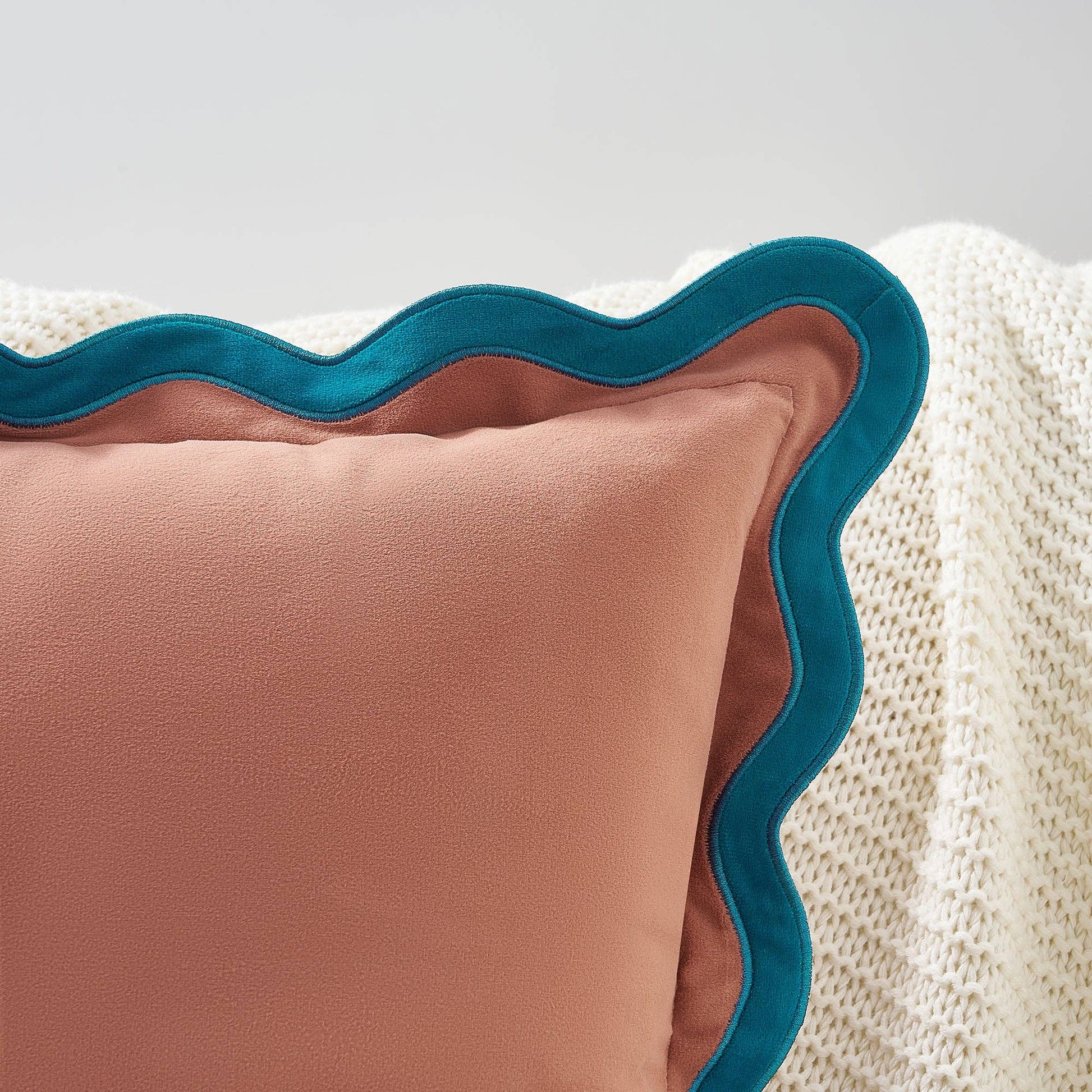 Pink pillow with teal scalloped edge on a textured surface