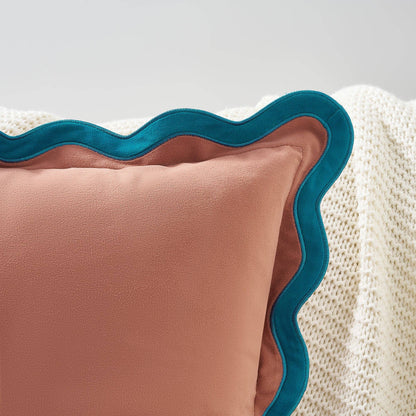 Pink pillow with teal scalloped edge on a textured surface