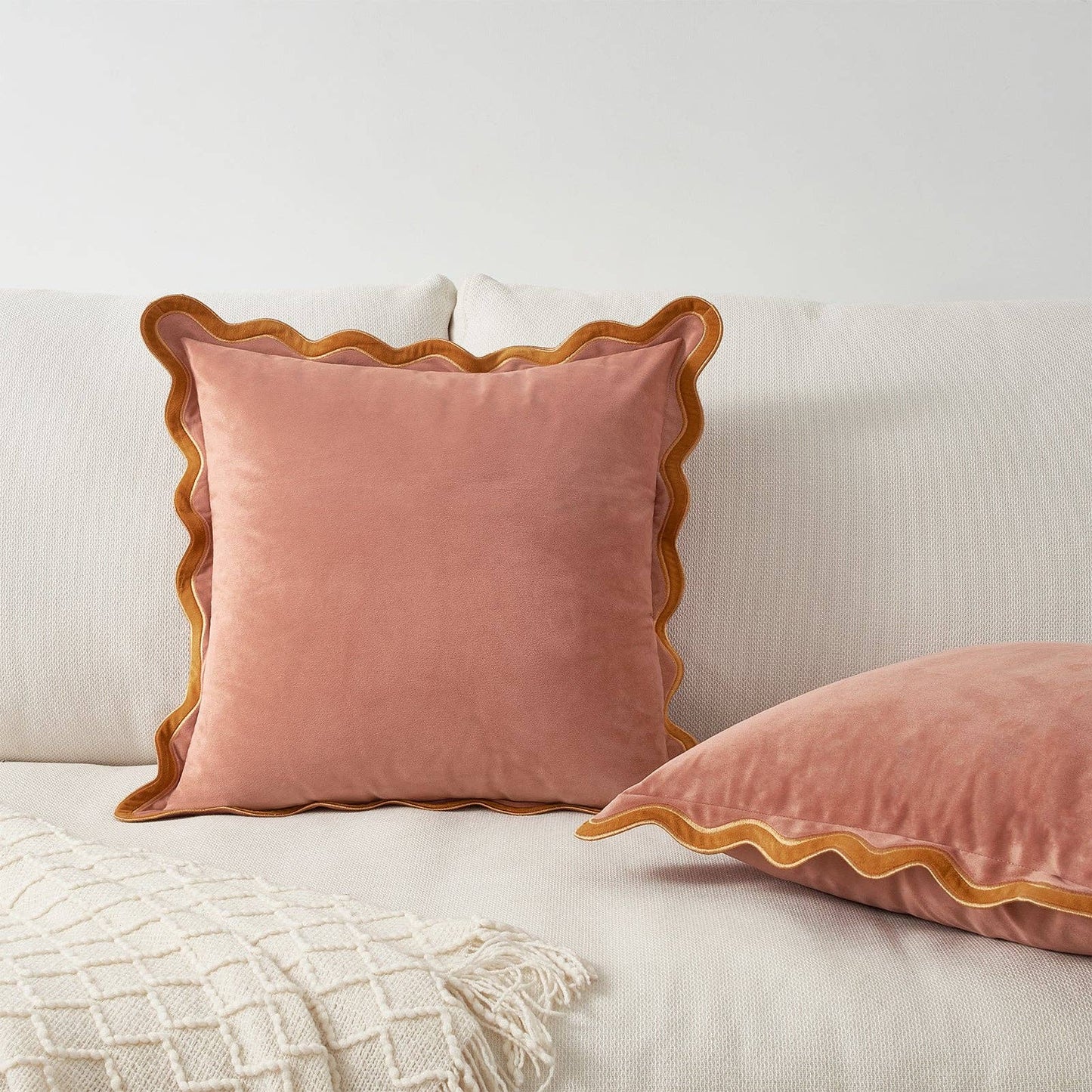 Pink velvet pillow with scalloped edge on a light-colored sofa.