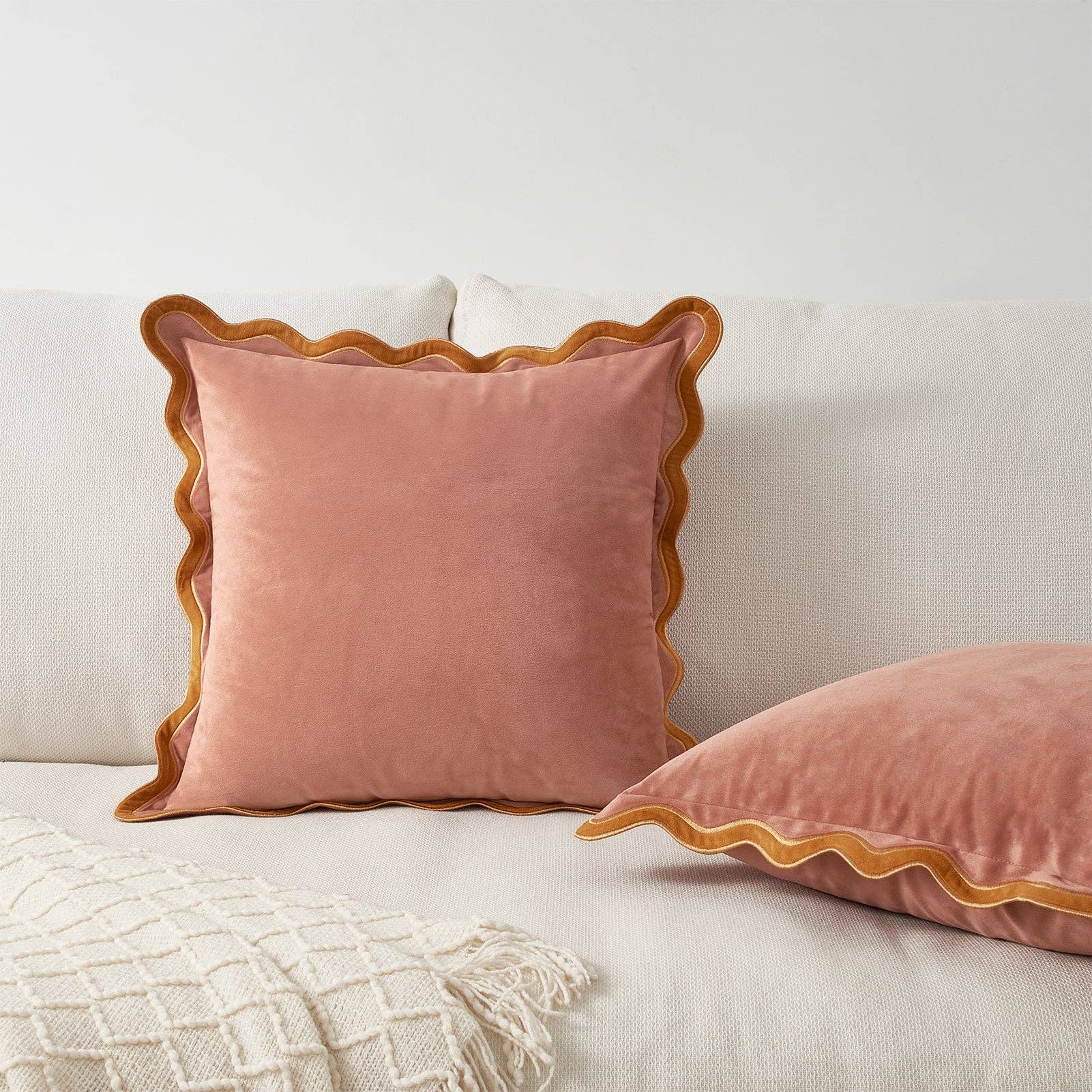 Pink velvet pillow with scalloped edge on a light-colored sofa.