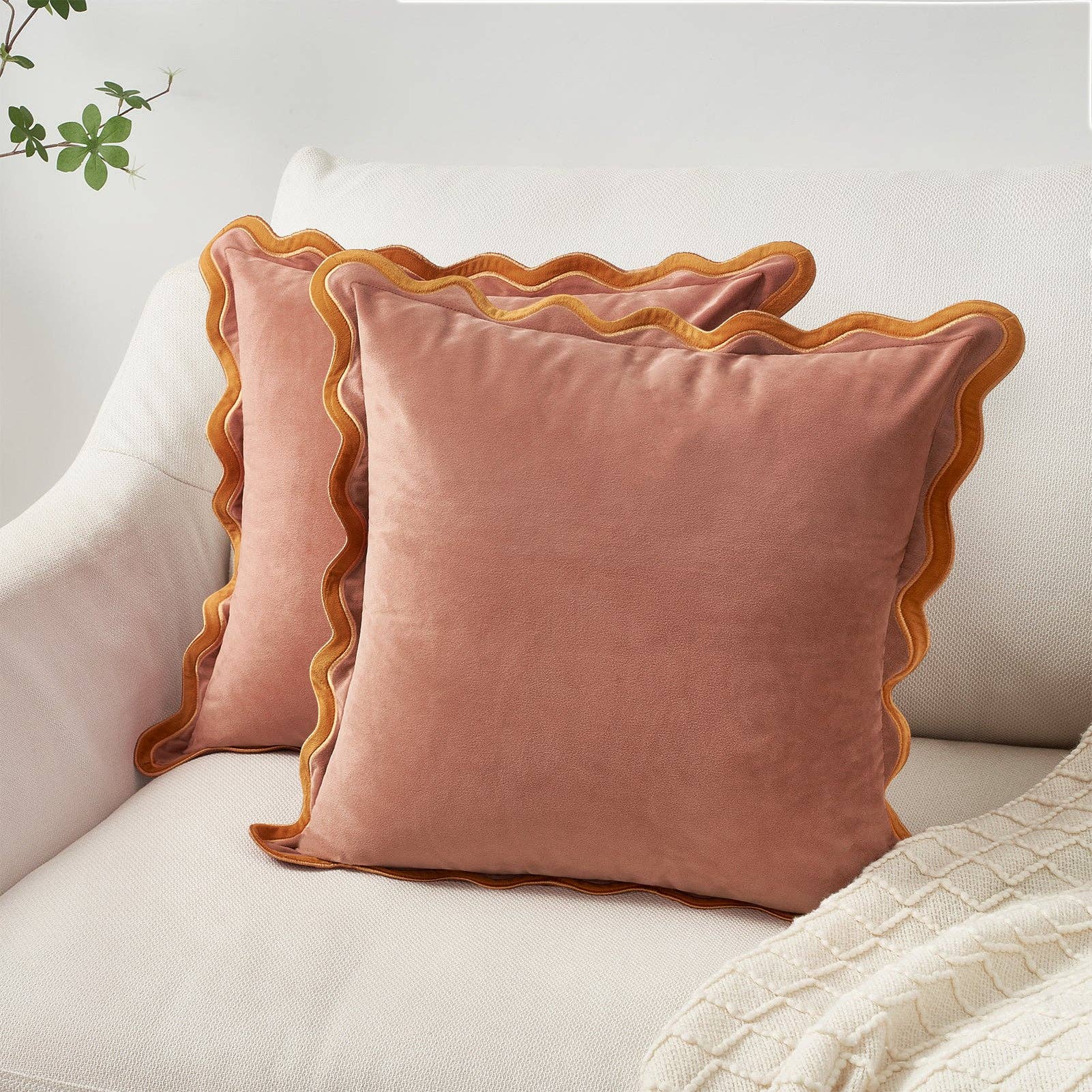 Pink velvet pillows with scalloped edges on a light-colored sofa.