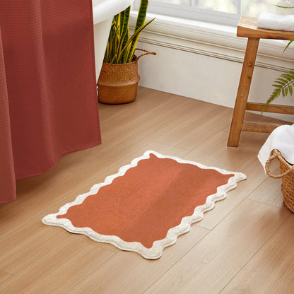 Red bath mat with white border on a wooden floor in a bathroom setting.