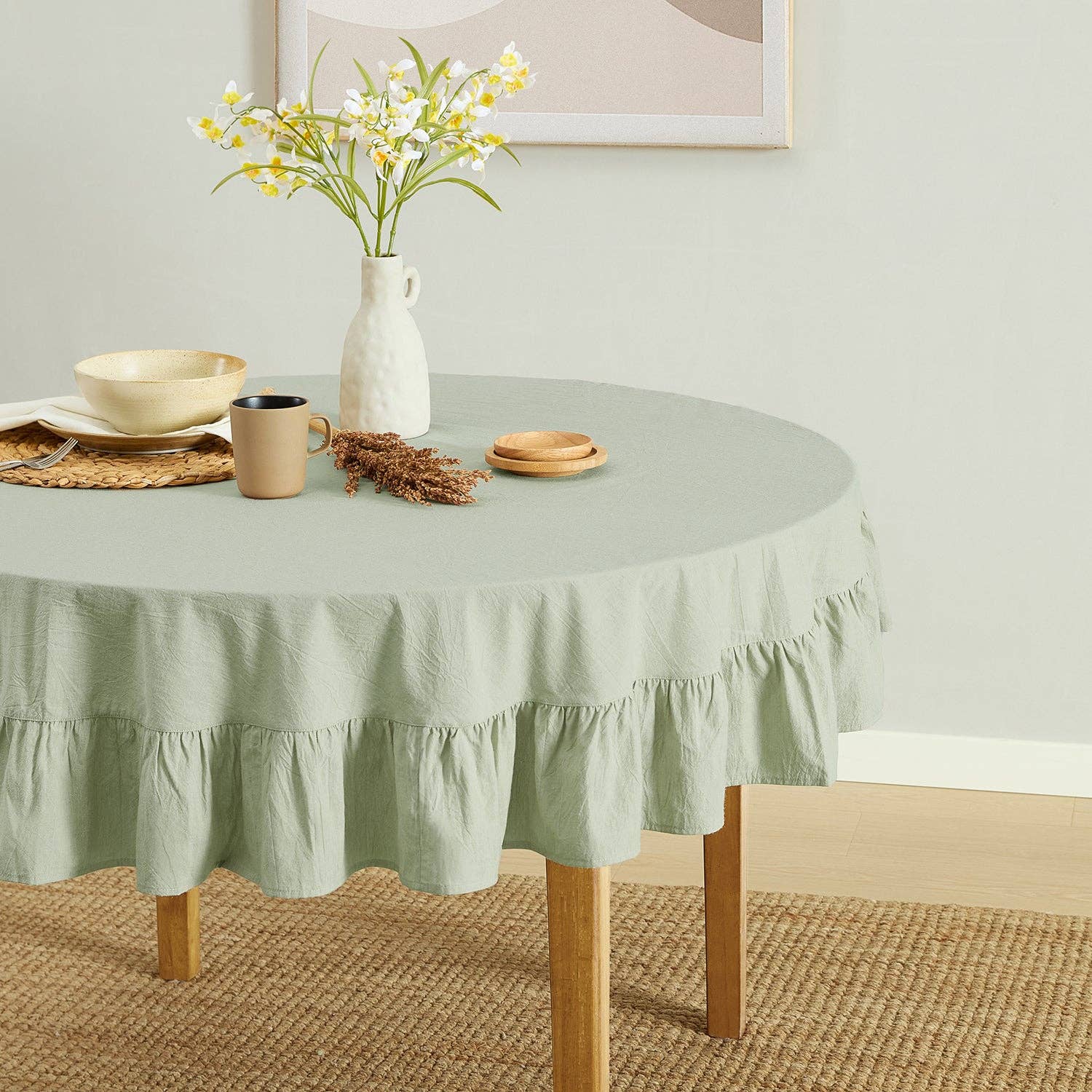 Round table with a green tablecloth, vase with flowers, and decorative items on a light-colored floor.