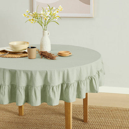 Round table with a green tablecloth, vase with flowers, and decorative items on a light-colored floor.