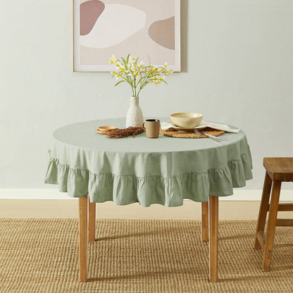 Round table with a green tablecloth, vase with flowers, and other decor items in a room.