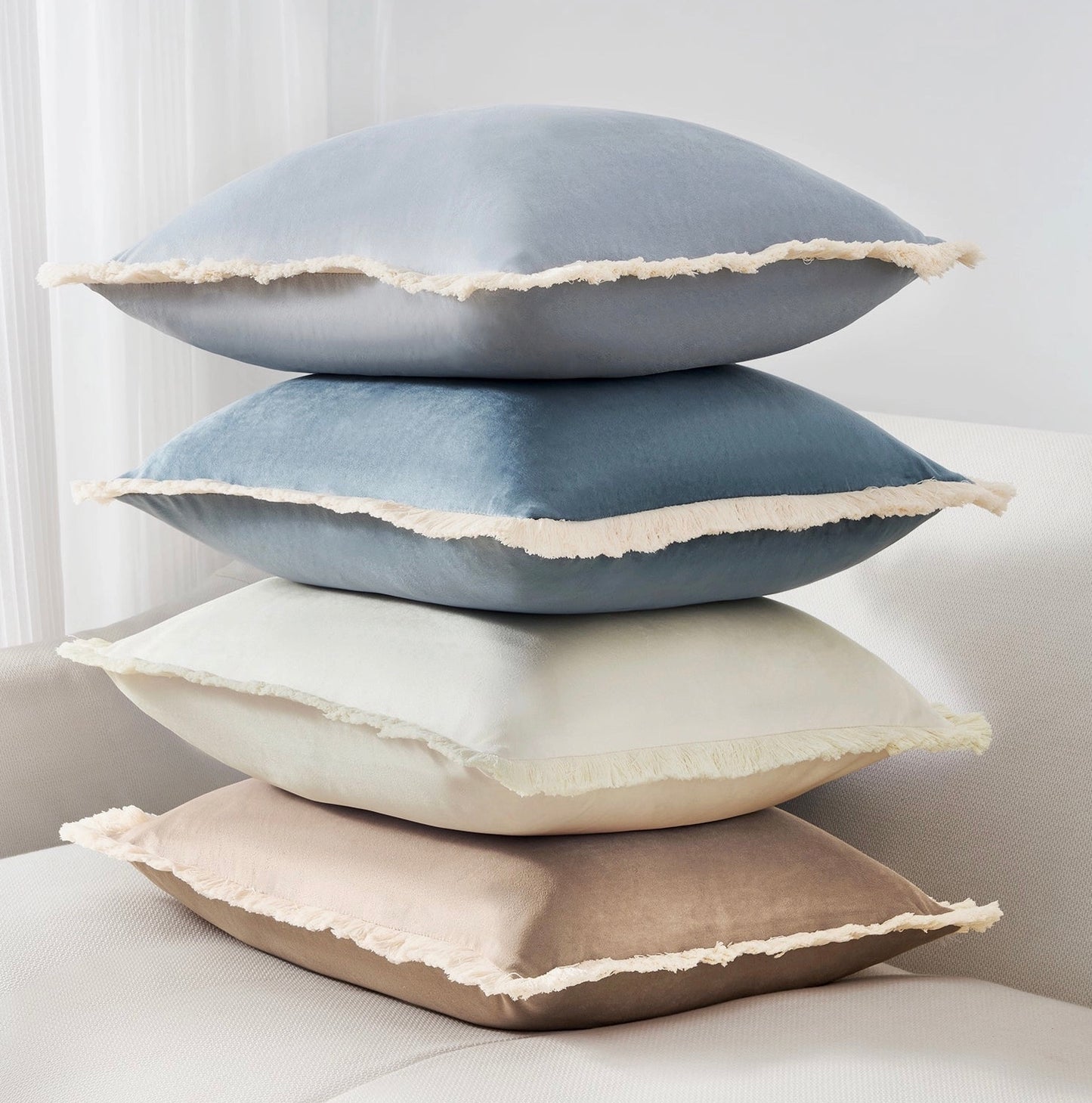 Stack of four decorative pillows in blue, gray, white, and beige on a neutral background.